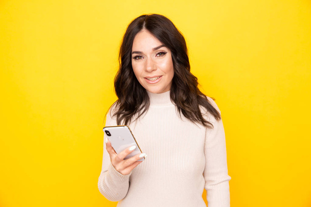 Portrait of female model holding mobile isolated the yellow background. - Photo, Image