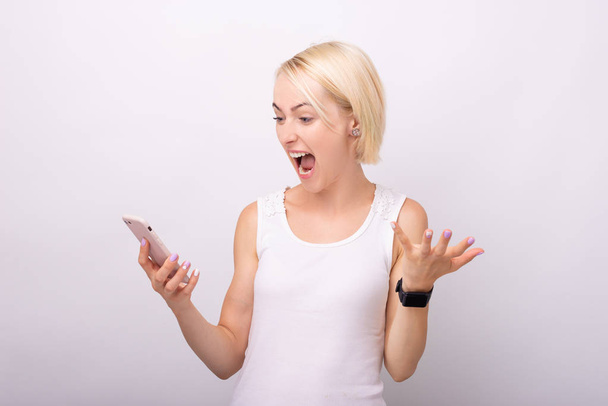 Photo  of a very excited young woman, screaming and holding a smartphone over isolated background   - Фото, изображение