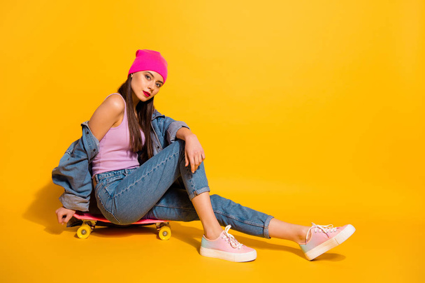 Full length side profile body size photo beautiful she her lady weekend vacation sporty sitting own skate board not smile wear casual jeans denim jacket shoes pink hat isolated yellow vivid background - Valokuva, kuva
