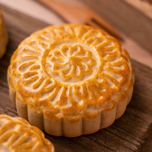 Round shaped moon cake Mooncake - Chinese style traditional pastry during Mid-Autumn Festival / Moon Festival on wooden background and tray, close up - Фото, изображение