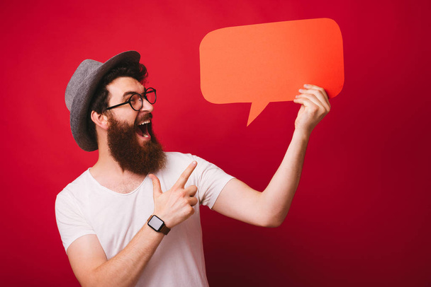 Photo of excited bearded guy, pointing at empty blank, over red isolated background  - Fotografie, Obrázek