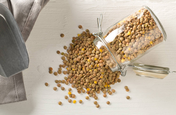 Raw, dry, uncooked brown lentil legumes in glass storage jar on  - Fotografie, Obrázek