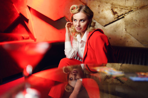 Photo of young blonde girl in red jacket sitting on sofa at table - Foto, imagen