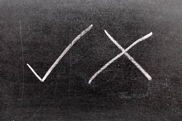 White color chalk hand drawing as check mark of right and wrong shape on black board background - Photo, Image