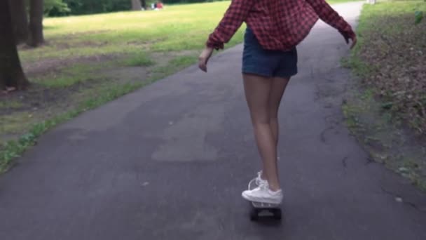νεαρό κορίτσι βόλτες με ένα σκέιτμπορντ στο δρόμο σε ένα καλοκαιρινό πάρκο σε αργή κίνηση - Πλάνα, βίντεο