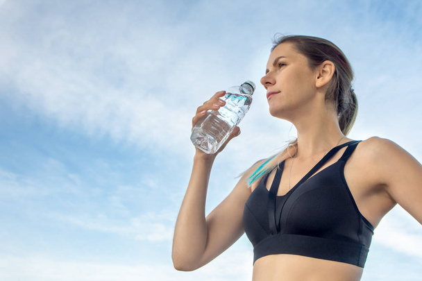 Porträt der jungen schönen dunkelhaarigen Fitness-Frau, die im sommergrünen Park Wasser trinkt. - Foto, Bild
