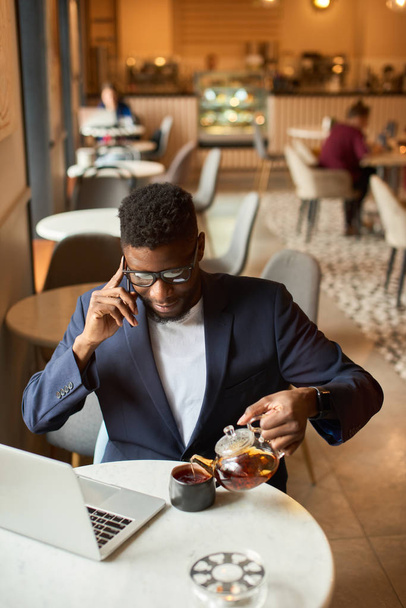 Afro-americano che lavora al portatile e si versa il tè
. - Foto, immagini