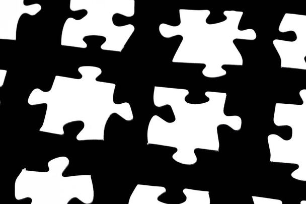 weiße Puzzleteile vor schwarzem Hintergrund mit einem gewissen Abstand zwischen den einzelnen Teilen - Konzept für Teilschritte oder Teilelemente eines großen Ganzen präsentiert mit Puzzleteilen  - Foto, Bild