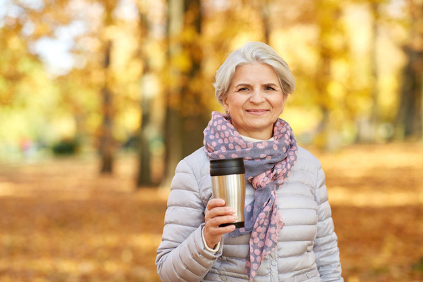old woman with hot drink in tumbler at autumn park - Фото, изображение