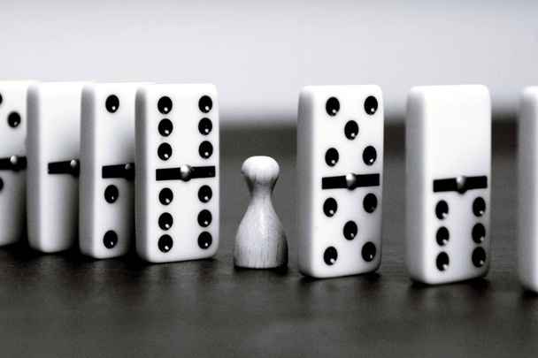 Um peão de madeira branco fica entre dominós alinhados e evita que o círculo vicioso ou a reação em cadeia continue conceito com dominós e jogando figuras como suporte criativo
  - Foto, Imagem