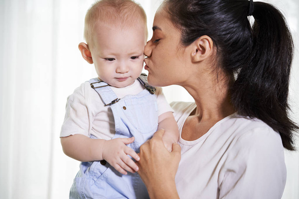 fröhliche junge Frau küsst ihren kleinen Sohn auf die Wange - Foto, Bild