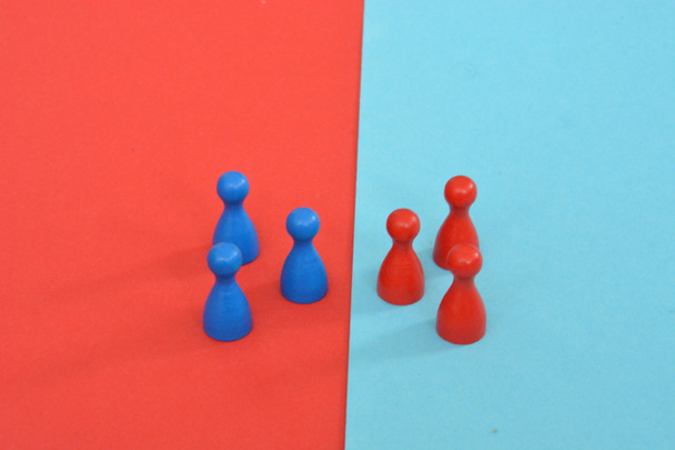 ein rotes und ein blaues Team von Holzspielfiguren eines Brettspiels stehen sich gegenüber und werden vom jeweils gegensätzlichen Hintergrund begrüßt - Konzept der Grenzen und Unterschiede  - Foto, Bild