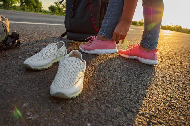 La mujer dejó los zapatos de trabajo y usó zapatillas de deporte en la carretera con la luz dorada del sol. Concepto de vacaciones y viajes
 - Foto, imagen