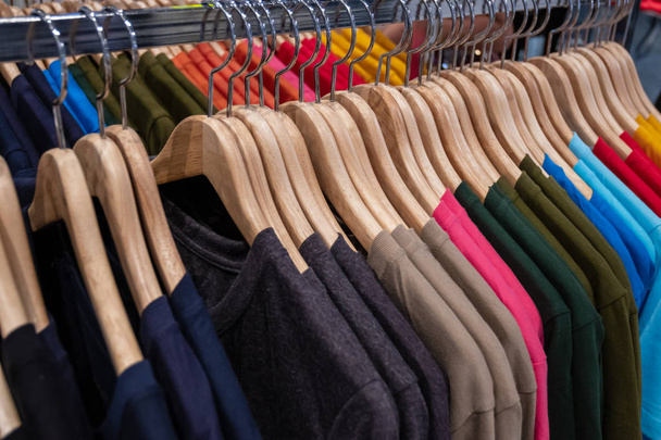 Mode-Kleidung auf Kleiderständern - bunte Kleiderschränke. Nahaufnahme der farbenfrohen Auswahl trendiger Männermode auf Kleiderbügeln im Kleiderschrank oder Einkaufszentrum. - Foto, Bild