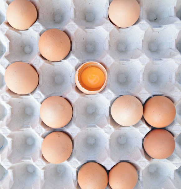 Na třicátých voštových vejcích leželo několik vajíček, jeden otevřený a vaječný žloutek je viditelný-jedno vajíčko se liší od zbytku krabice, protože je rozbitý koncept individuální stravy s vejci - Fotografie, Obrázek