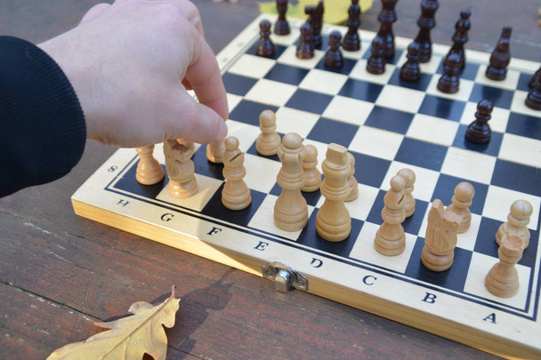 Un tablero de ajedrez con piezas de ajedrez está de pie sobre una mesa de madera en el bosque de otoño con hojas coloridas de otoño al lado - dos piezas de ajedrez se enfrentan entre sí y causan una pelea con los respectivos equipos
 - Foto, imagen
