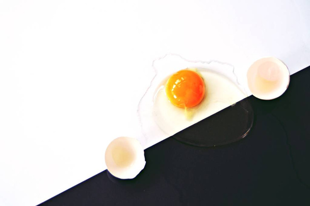 ein geöffnetes Ei mit intaktem Eigelb umgeben von Eiweiß liegt auf einem halb schwarzen halb weißen Hintergrund - Konzept mit Schwarz-Weiß und einem Ei  - Foto, Bild