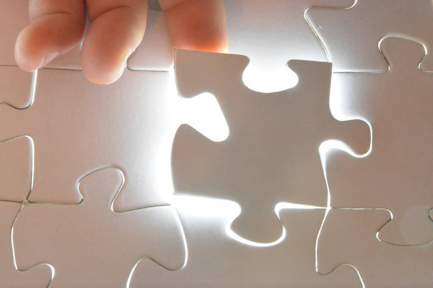 Közeli fel egy kézzel elhelyezés egy fehér Puzzle-darabot a teljes puzzle. A felület a hiányzó rész ragyog fényesen-Concept bemutatása a ragyogó sikere befejezett projekt  - Fotó, kép