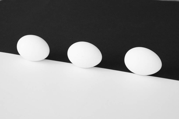 白いカップを持つ鶏の卵は、半分の白と半分の黒の背景の前に横たわっている - 白い卵と少し影の背景として強いコントラストを持つコンセプト - 写真・画像