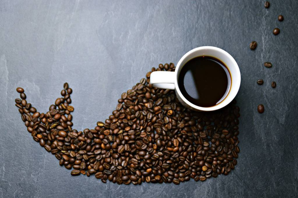 Koffiebonen op een zwarte achtergrond vormen het silhouet van een walvis en twee kopjes koffie vormen hun ogen-concept met koffie en walvis  - Foto, afbeelding