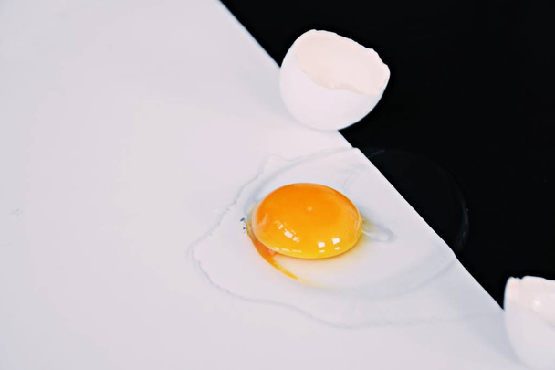 An opened egg with intact egg yolk surrounded by egg whites lies on a half black half white background - concept with black and white and an egg  - Valokuva, kuva