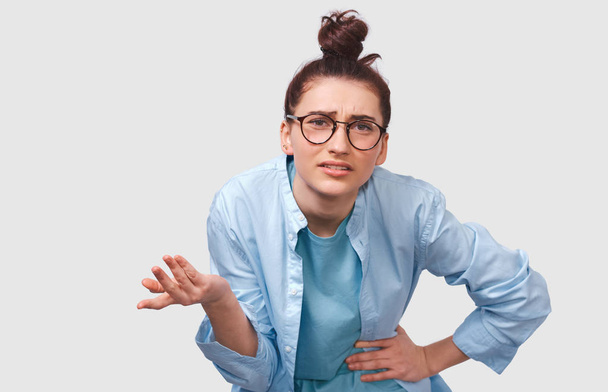 Displeased young woman, looking doubtful at discussing important decisions, gesturing with hand, dressed in casual trendy outfit, posing over white wall. Student girl has confused expression.  - Photo, Image