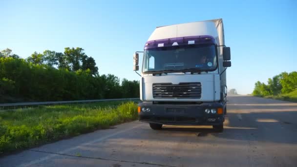 晴れた日に商品を輸送する高速道路上で運転貨物トレーラーとトラックの正面図。田舎道を走るローリー。美しい自然の背景。ロジスティクスコンセプト。スローモーションクローズアップ - 映像、動画