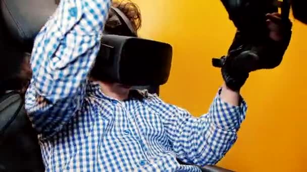 Child boy holding gaming computer wheel getting experience using VR-headset glasses of virtual reality in the game club - Footage, Video