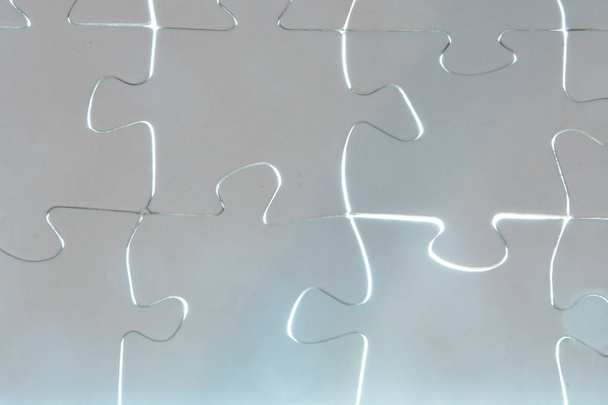 Κοντινό κομμάτι ενός χεριού βάζοντας ένα κομμάτι λευκού παζλ σε ένα συνολικό παζλ. Η επιφάνεια του τμήματος που λείπει λάμπει έντονα-έννοια για την παρουσίαση της ακτινοβόλο επιτυχία ενός ολοκληρωμένου έργου  - Φωτογραφία, εικόνα