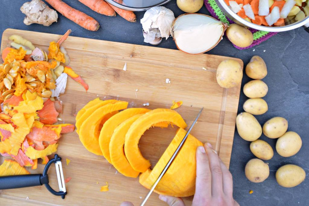 Cortar verduras para zanahorias, papas, cebollas, ajo y una calabaza para sopa de calabaza en una tabla de madera y verter en la olla - primer plano en las manos desde arriba
  - Foto, Imagen