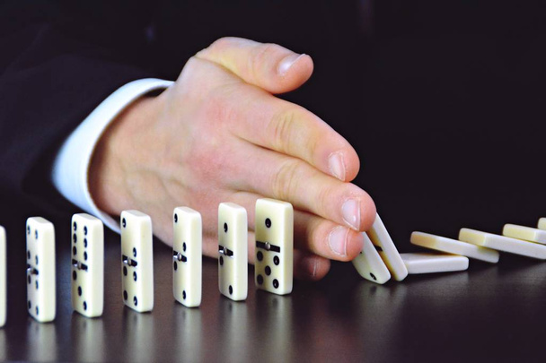 Close-up of a hand of a young businessman examining a disturbance factor in an otherwise perfectly functioning chain reaction from dominoes - symbolic of the complexity of leadership decisions  - 写真・画像