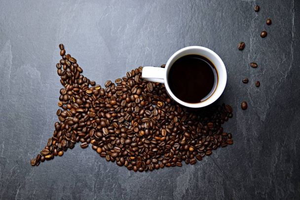 Os grãos de café em um fundo preto formam a silhueta de uma baleia e duas xícaras de café formam seus olhos - conceito com café e baleia.
  - Foto, Imagem