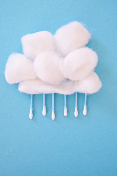 Cotton labdát, mint egy gyapjú és fülbotokkal, mint az eső vagy hó, a kék háttér-koncepció az eső vagy gyors pamut tamponok és pamut labdák - Fotó, kép