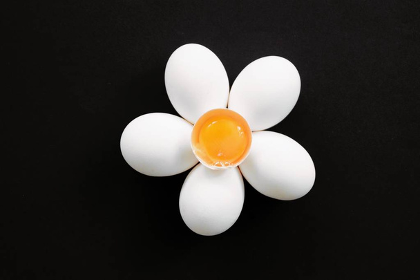 A flower of white eggs with a black background and an egg whipped with egg yolk in the center as a blossom - concept with fresh eggs and dark background - Photo, image
