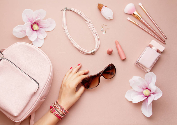 ピンクの女性アクセサリーとバックパックとサングラスを持つ女性の手でフラットレイ。夏のファッショントレンド、ショッピングのアイデア - 写真・画像