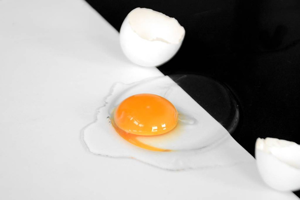 ein geöffnetes Ei mit intaktem Eigelb umgeben von Eiweiß liegt auf einem halb schwarzen halb weißen Hintergrund - Konzept mit Schwarz-Weiß und einem Ei  - Foto, Bild
