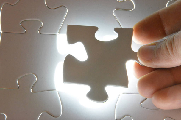 Close-up of a hand putting a white puzzle piece in a total puzzle. The surface of the missing part shines brightly - Concept for the presentation of the radiant success of a completed project  - Photo, Image