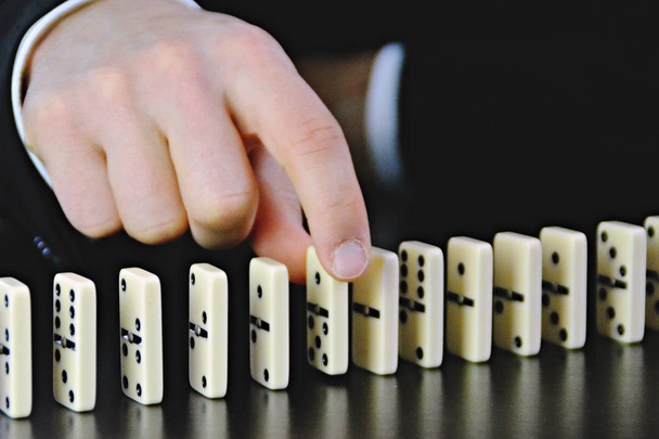 Close-up of a hand of a young businessman examining a disturbance factor in an otherwise perfectly functioning chain reaction from dominoes - symbolic of the complexity of leadership decisions  - Photo, Image