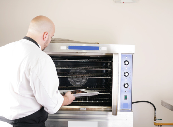 Шеф-повар кладет поднос сочного стейка в профессиональную духовку
 - Фото, изображение