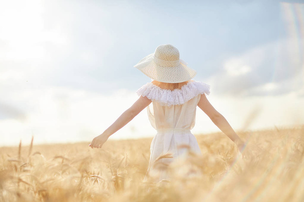 昼間の小麦畑で腕を上げた帽子をかぶった白人女性 - 写真・画像