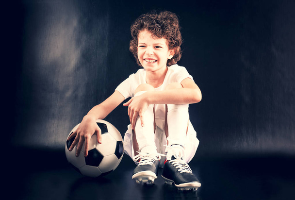 Täyspitkä muotokuva poika urheiluvaatteet poseeraa jalkapallo tummalla pohjalla. Kopioi tila
. - Valokuva, kuva
