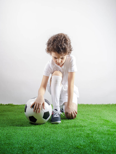 Disappointed little footballer sitting on the grass. Copy space - Zdjęcie, obraz