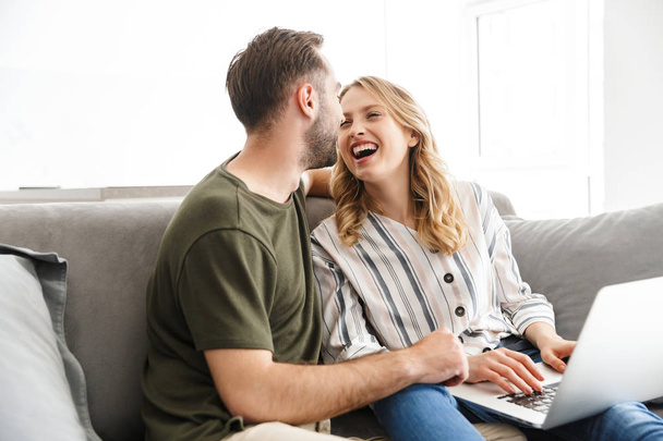 Happy excited young loving couple sitting on sofa at home using laptop computer. - Foto, immagini