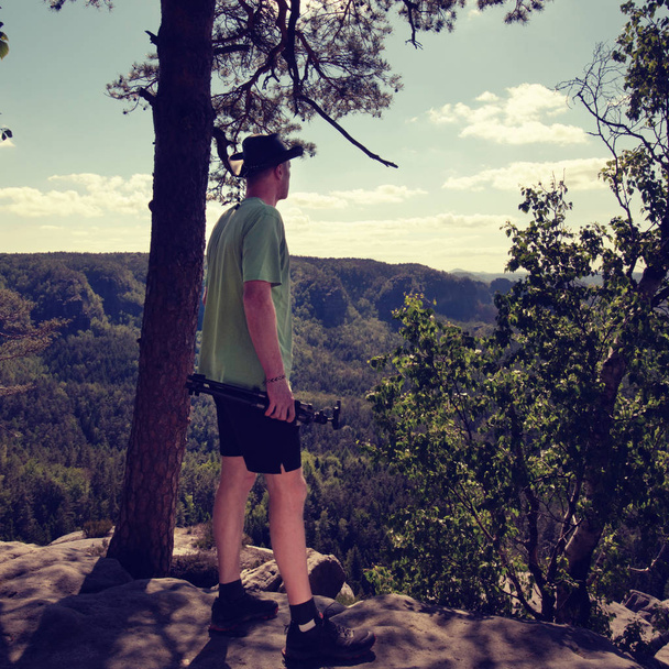 Красивый мужчина позирует на скале в футболке и ковбойской шляпе
 - Фото, изображение
