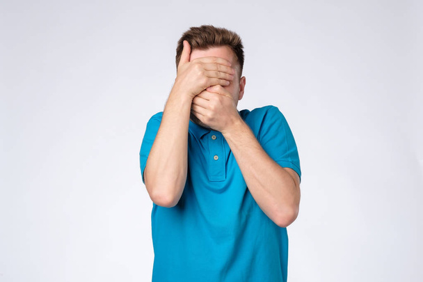 Jovem caucasiano homem de camisa azul fecha o rosto com as mãos tentando ficar anônimo
. - Foto, Imagem