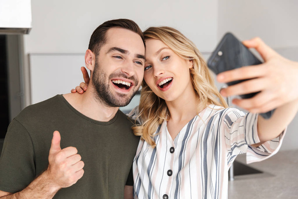 Happy young loving couple posing at the kitchen at home hugging take a selfie. - Foto, Bild