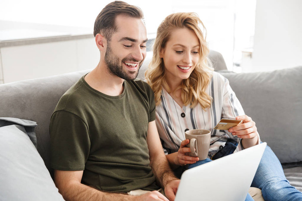 Happy excited young loving couple sitting on sofa at home using laptop computer. - Foto, Bild
