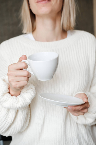 Woman in white knitted sweater holding cup of coffee. Female hands with cup of tea. Close up - Fotó, kép