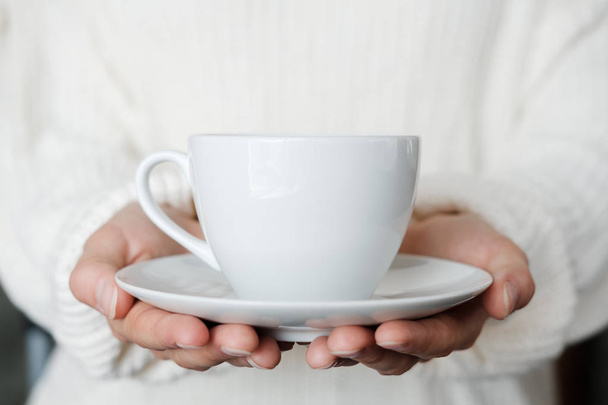 Frau in weißem Strickpullover mit Tasse Kaffee. Frauenhände mit einer Tasse Tee. Nahaufnahme - Foto, Bild