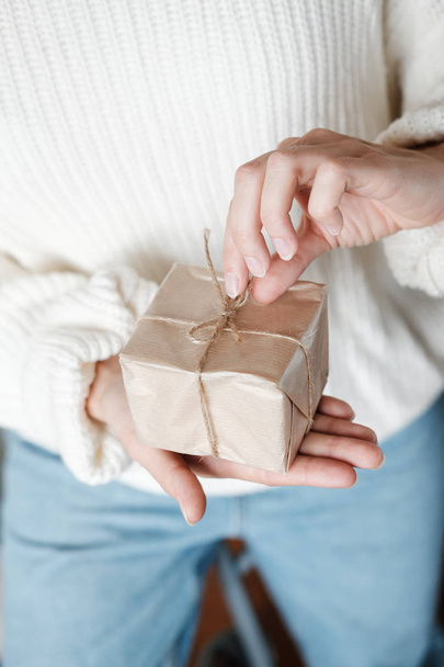 Woman in white knitted sweater giving wrapped gift.  Close up Female hands holding Christmas box present. Christmas, New Year, shopping, preparation on Winter Holidays, donation concept. Vertical - Zdjęcie, obraz